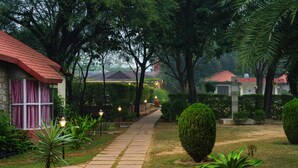 A pathway leading to a building with a red roof, surrounded by lush greenery and well-maintained lawns. - Sariska Tiger Heaven Resort (Thanagazi)