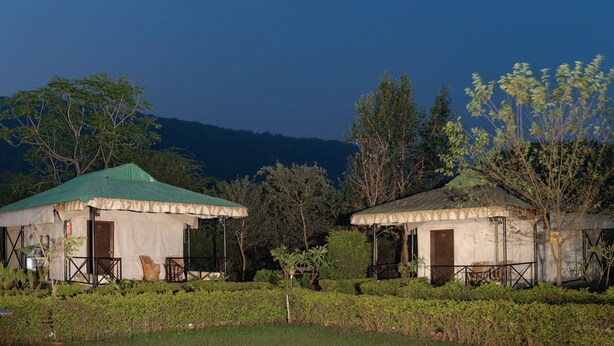 Two tents with green roofs, surrounded by greenery and trees, set against a mountainous backdrop. - Sariska Tiger Heaven Resort (Thanagazi)