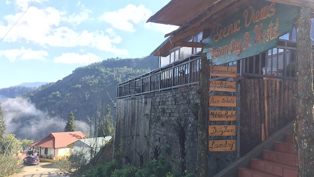 A rustic building with a signboard listing amenities like scenic views, farmstay, hostel, accommodation, cafe, restaurant, bus tickets, motoclub rental, daily tours, and laundry. - Scenic Views Farmstay & Hostel (Sa Pa)