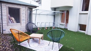 A patio with a small table and two chairs, a covered seating area, and a green artificial turf lawn.