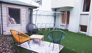 A patio with a small table and two chairs, a covered seating area, and a green artificial turf lawn.