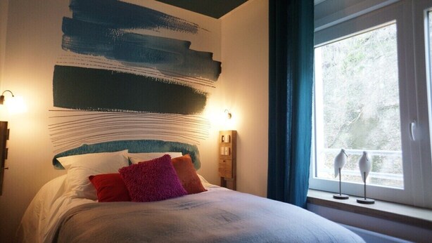 A bedroom with a large bed, a wall with abstract art, bedside lamps, and a window with curtains.