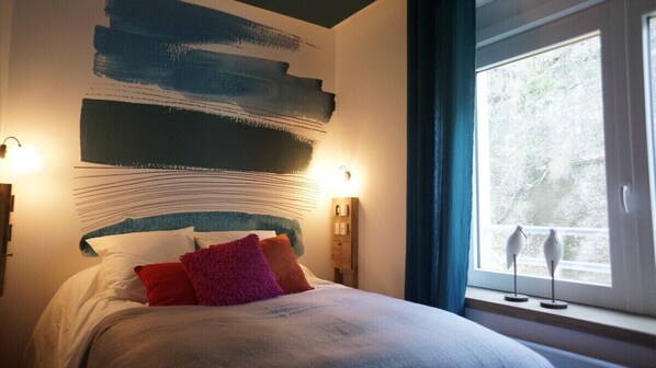 A bedroom with a large bed, a wall with abstract art, bedside lamps, and a window with curtains.