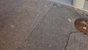 A clean, empty hallway with a metal grate on the floor, a fire extinguisher, and a security camera on the wall.
