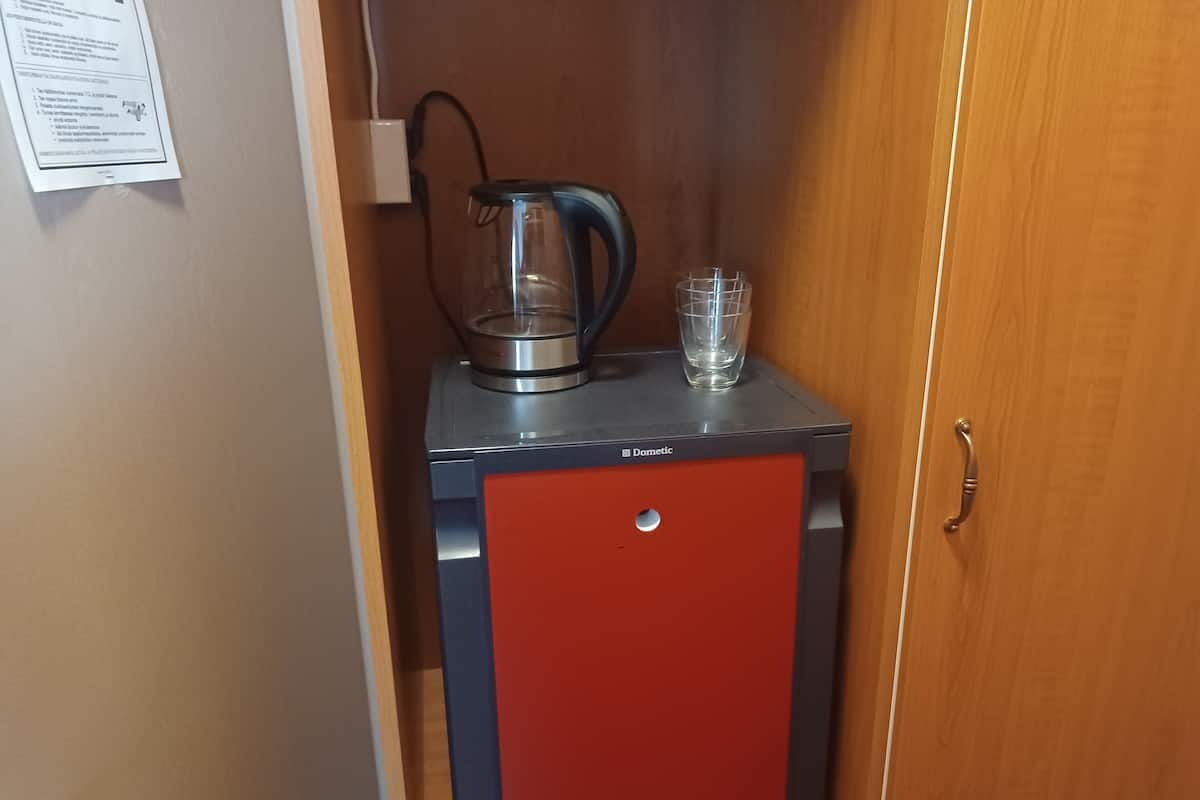 A compact kitchenette with a coffee maker, a glass, and a red cabinet.