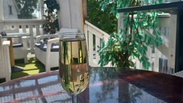 Un verre de vin blanc sur une table dans une pièce baignée de lumière, avec vue sur la verdure et un bâtiment en arrière-plan.
