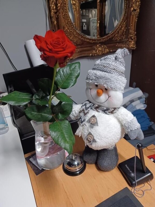 Un bureau sur lequel se trouve un vase contenant une rose rouge, un bonhomme de neige en peluche et une petite cloche.