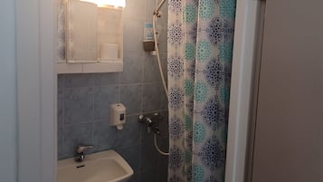 A bathroom with a sink, a toilet paper holder, a shower curtain, and a towel rack.