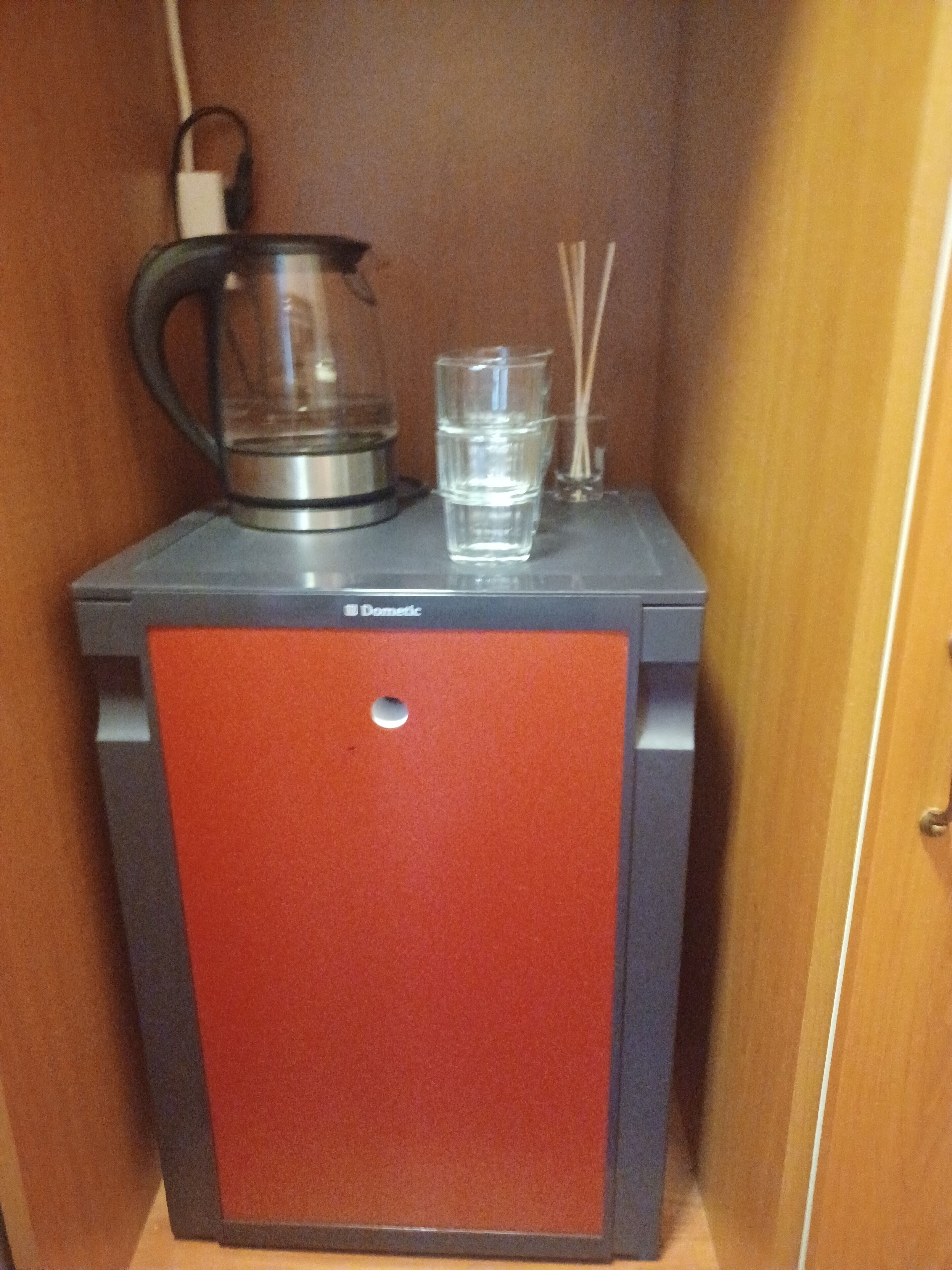 A compact kitchenette with a coffee maker, a glass of water, and a small container of tea or coffee sachets.