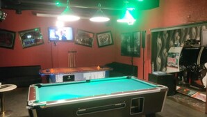 A pool table with a green felt surface, surrounded by a red wall with framed pictures and a television mounted above it. - Hotelli Ikahani  (Ikaalinen)