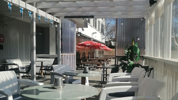 An outdoor patio area with white wicker furniture, tables, and a red umbrella. - Hotelli Ikahani  (Ikaalinen)