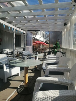 Un espace extérieur aménagé en terrasse, avec des meubles en osier blanc, des tables et un parasol rouge.