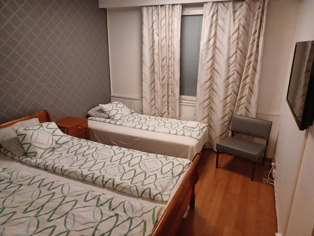 A bedroom with two beds, a small table, a bench, and a TV mounted on the wall.
