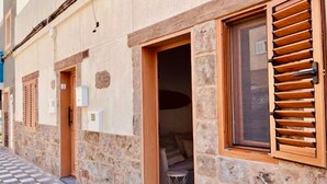 A stone building with a checkered floor, wooden shutters, and a small stool outside. - Click & Guest - Casa Mama Carina B (Agüimes)