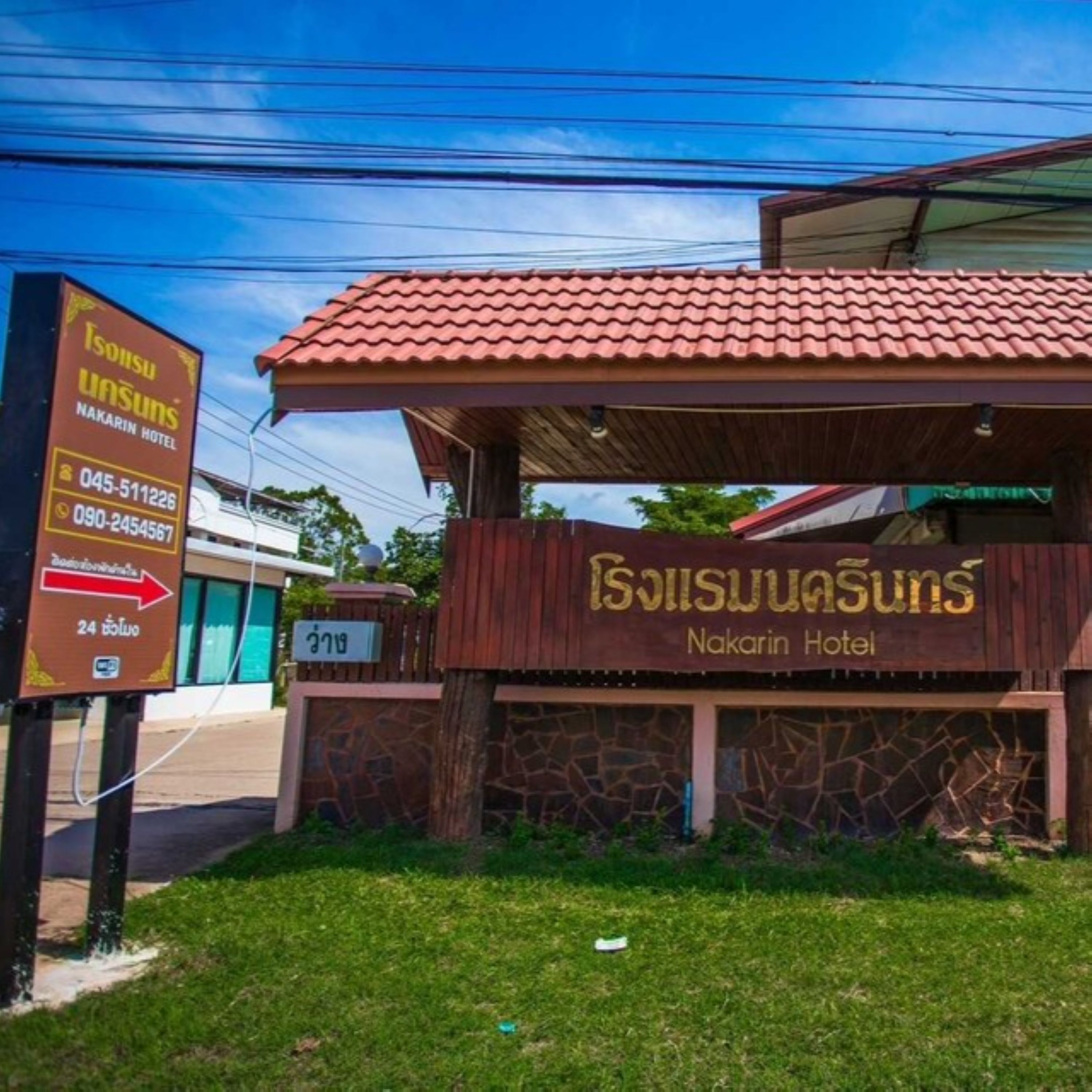 A hotel entrance with a red-tiled roof and a signboard displaying the hotel's name and contact numbers.
