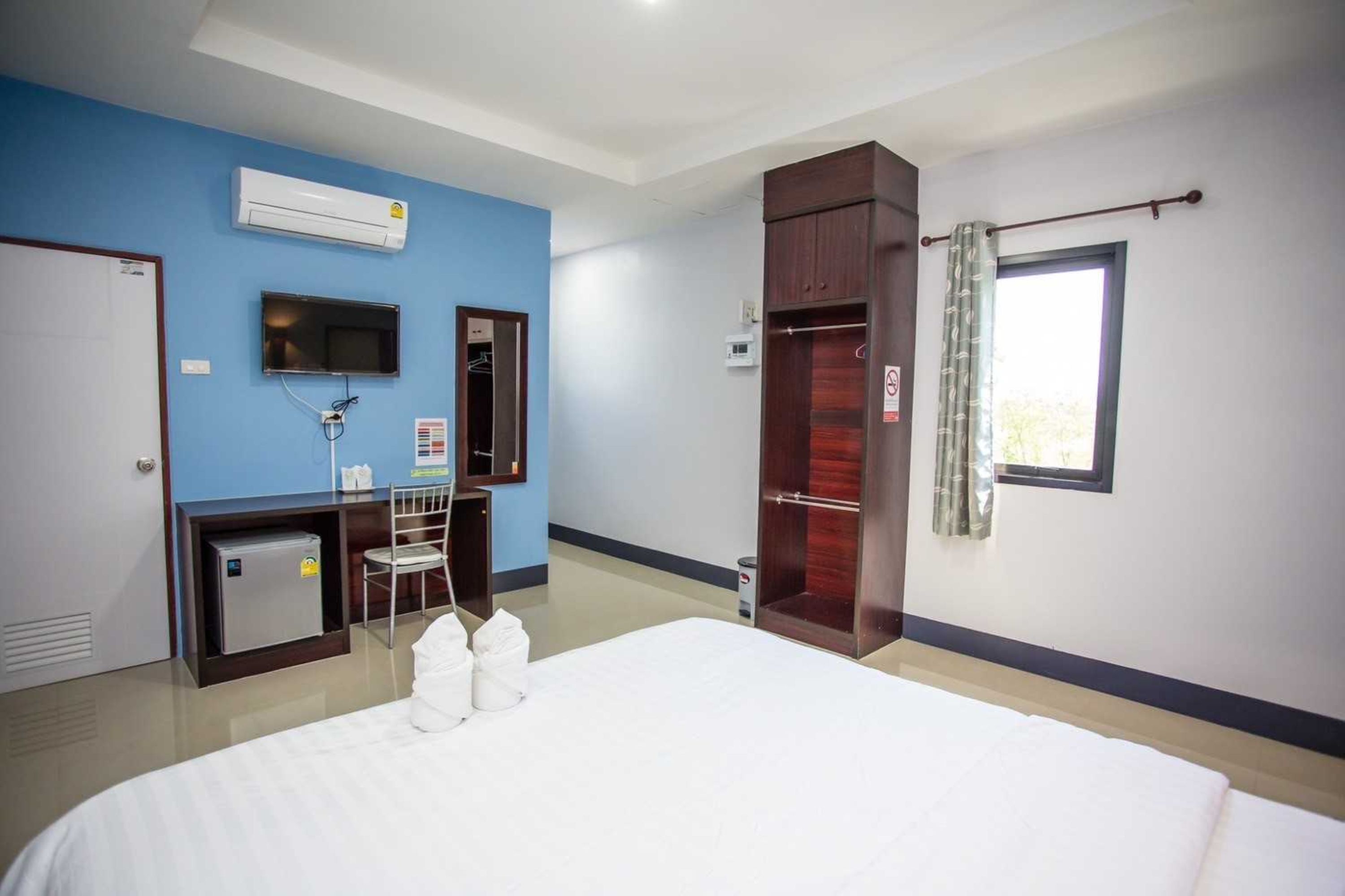 A hotel room with a bed, a desk with a chair, an air conditioner, a television, a wardrobe, and a window with curtains.