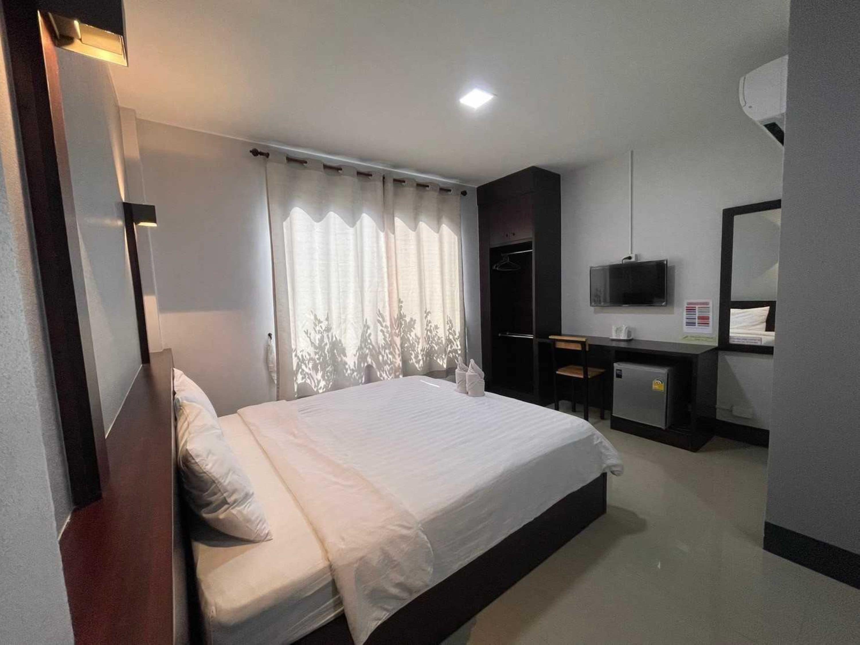 A hotel room with a bed, a desk, a chair, a TV, and a wardrobe.