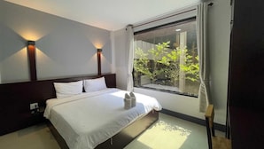 Een moderne hotelkamer met een groot bed, twee bedlampen, een raam met uitzicht op groen en een klein tafeltje met een stoel.
