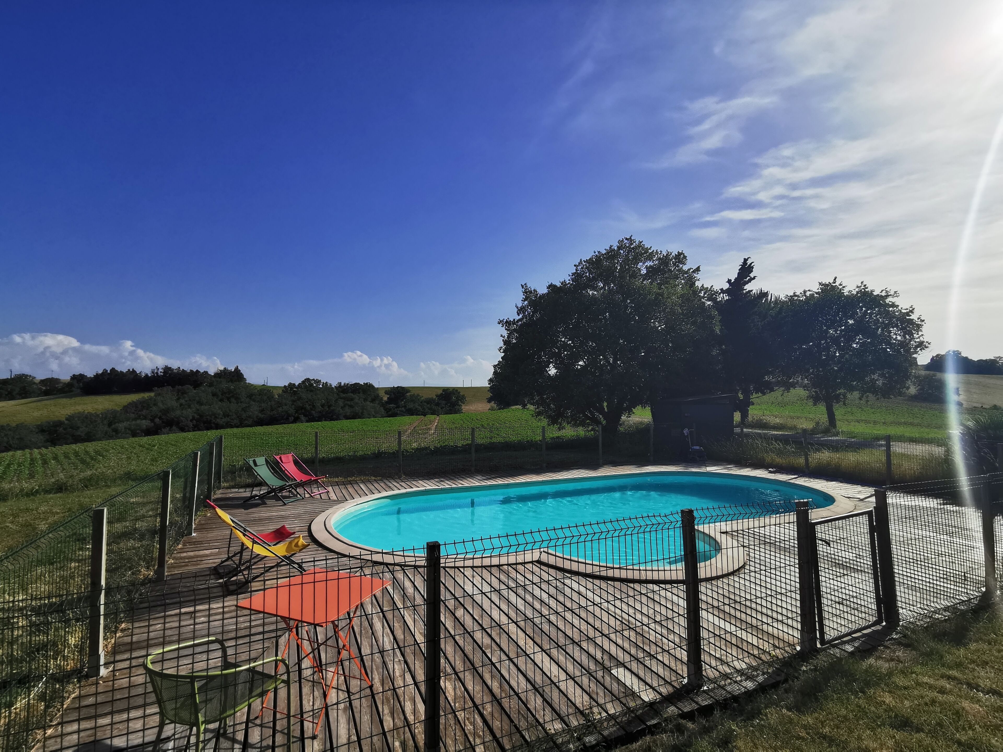 A swimming pool with a fenced deck, surrounded by a grassy area and trees.
