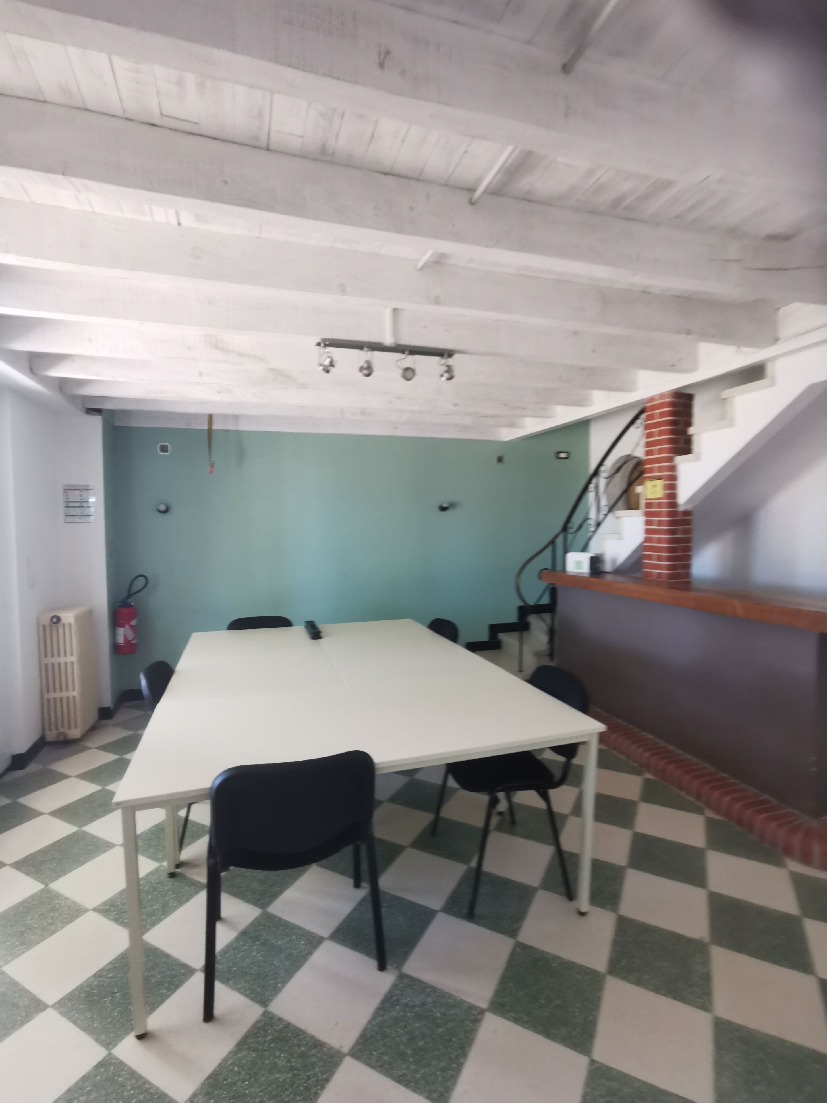 A conference room with a white table, black chairs, a checkered floor, a staircase, and a fire extinguisher.