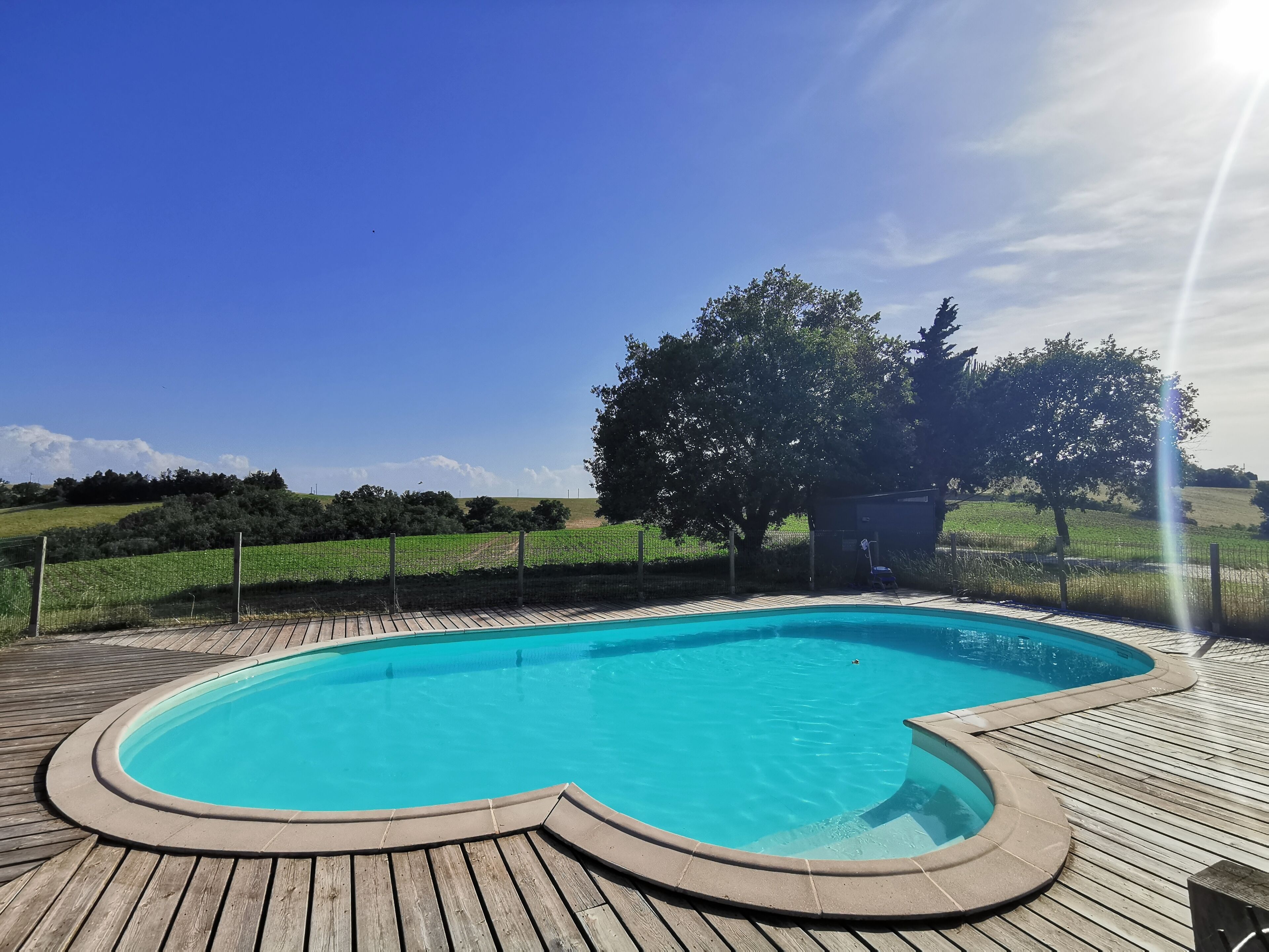 Una piscina con un muelle de madera, rodeada por una cerca y árboles.