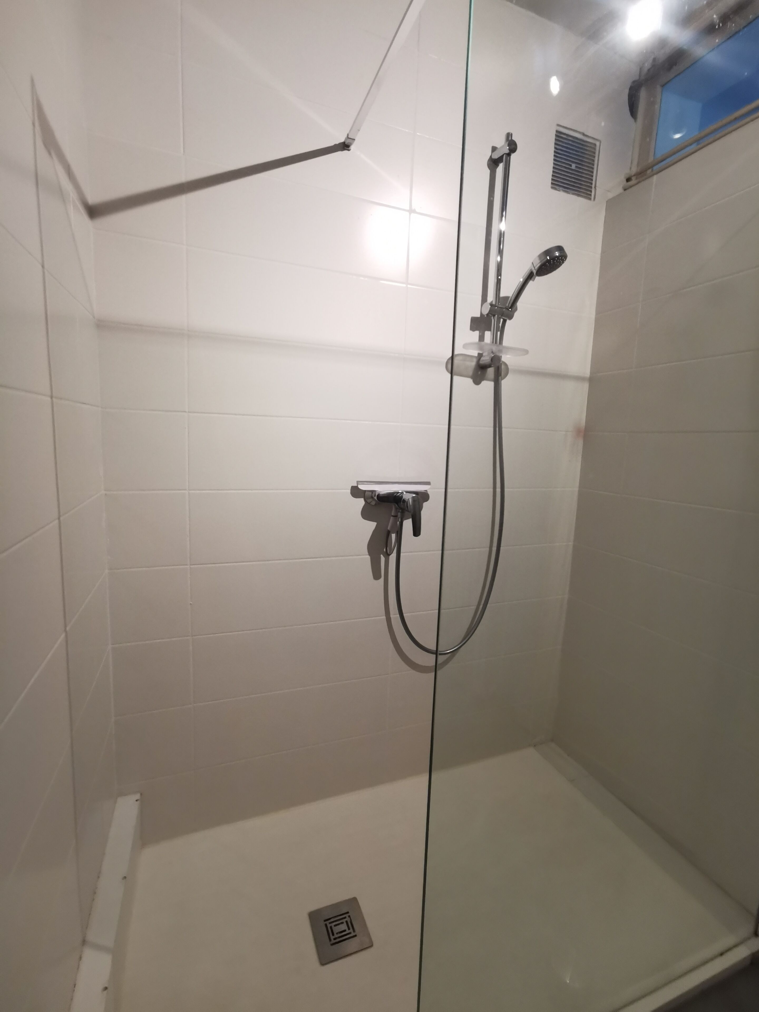 A glass-enclosed shower stall with a handheld showerhead, a wall-mounted faucet, and a control panel.