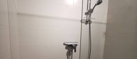 A glass-enclosed shower stall with a handheld showerhead, a wall-mounted faucet, and a control panel.