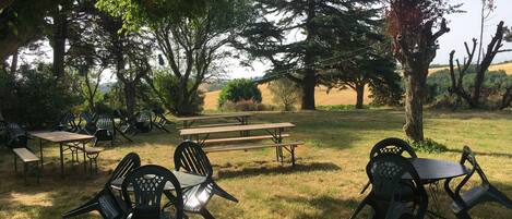 An outdoor seating area with picnic tables and chairs, surrounded by trees and a view of the countryside.