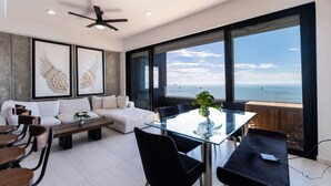 Ein modernes Wohnzimmer mit einem Glastisch, einer Couch und einem großen Fenster mit Meerblick.