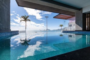 Uma piscina infinita com águas azul-claras, palmeiras e vista para o oceano e montanhas.