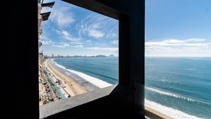 Blick aufs Meer vom Fenster aus, mit Strand, einer Straße und geparkten Autos.