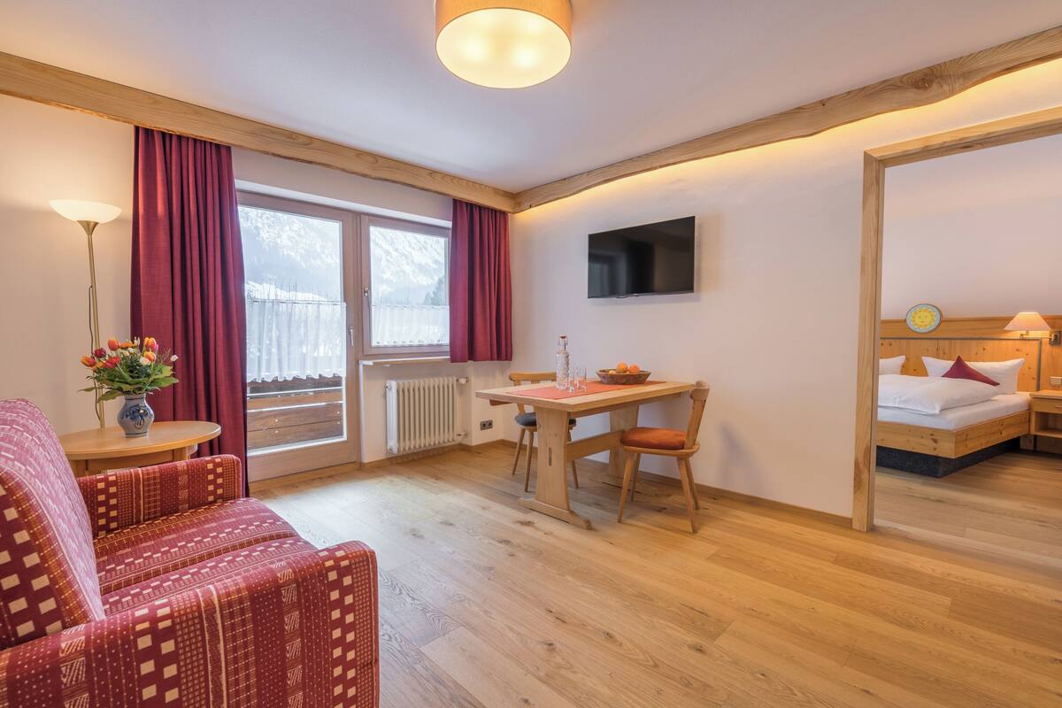 A cozy room with a sofa, a dining table, a TV, and a bed.
