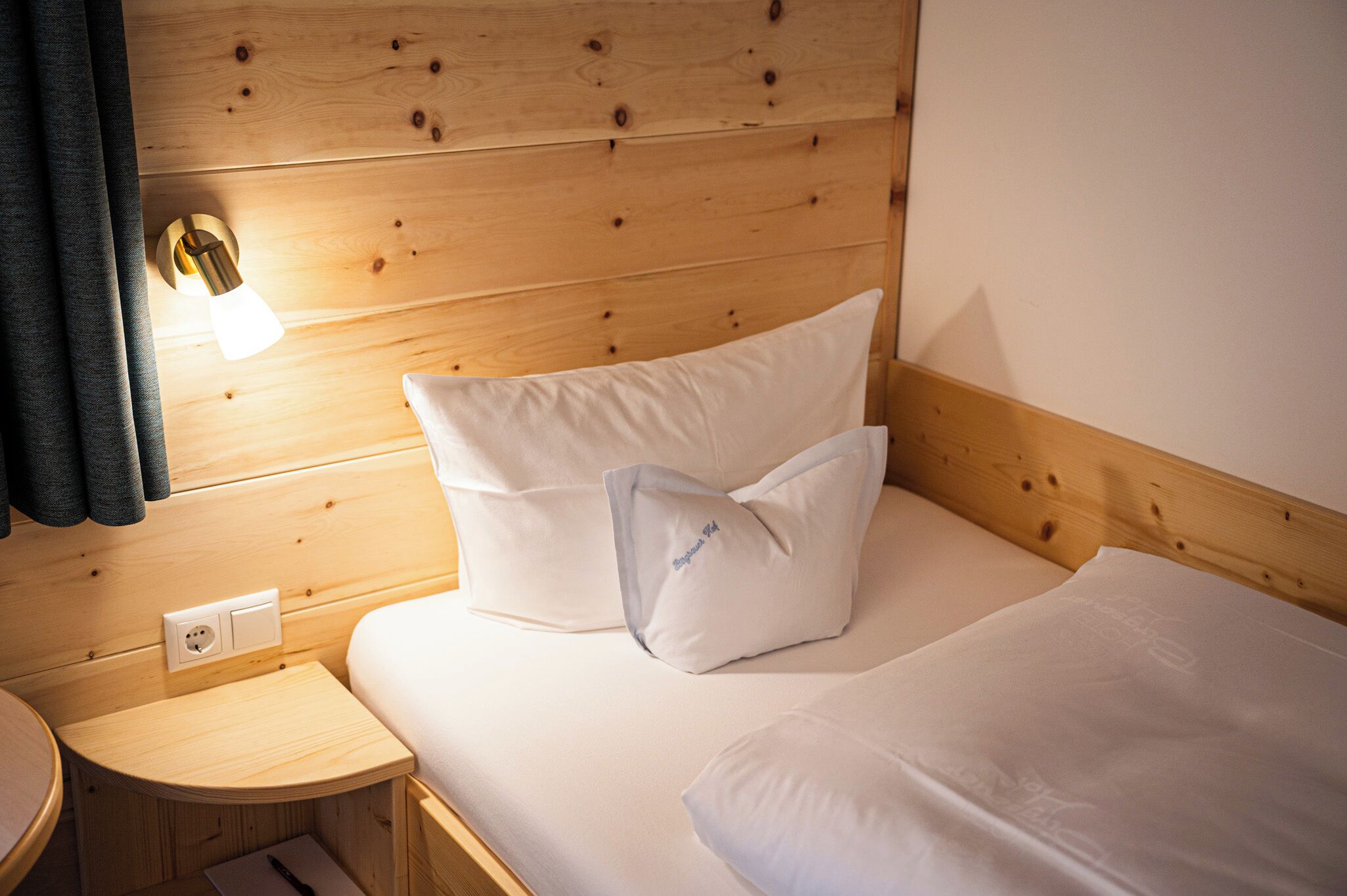 A wooden cabin-style room with a bed, a nightstand, and a wall-mounted light.