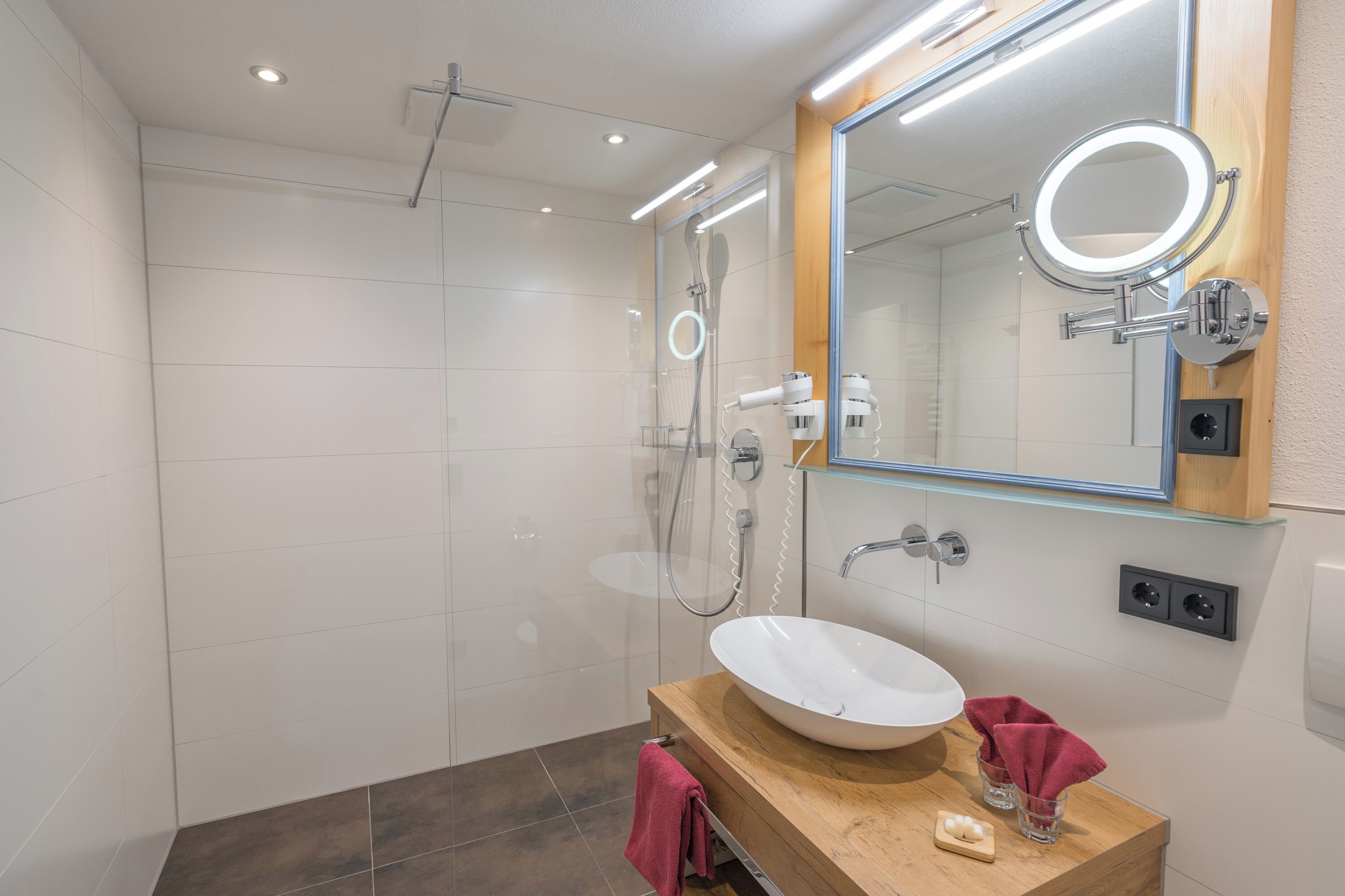 A modern bathroom with a glass-enclosed shower, a wooden vanity with a white sink, and a large mirror with a built-in light.