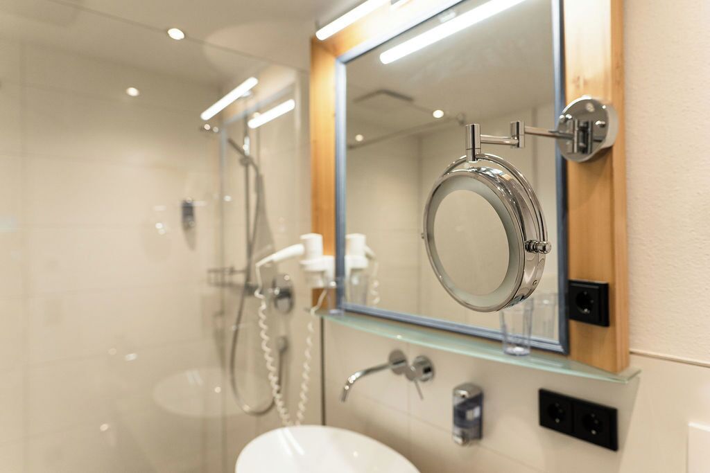Un baño moderno con ducha envuelta en vidrio, un espejo grande y un lavabo blanco.