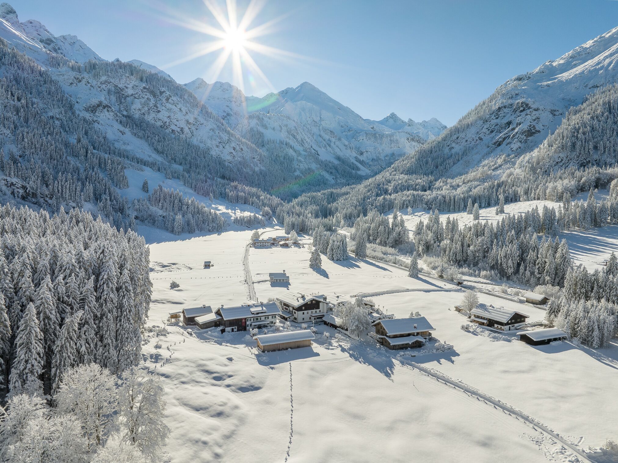 Un village de montagne enneigé, avec plusieurs bâtiments en bois, un ciel dégagé et un soleil brillant.