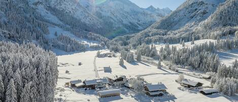 Un village de montagne enneigé, avec plusieurs bâtiments en bois, un ciel dégagé et un soleil brillant.