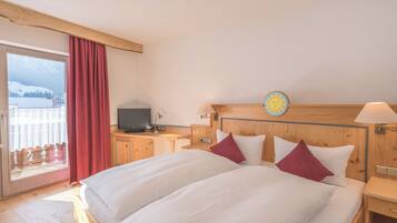 Habitación de hotel con una cama grande, cabecera de madera, un televisor sobre una mesa de madera y vistas a las montañas a través de una ventana.