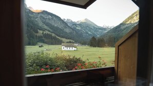 Vista desde una ventana con paisaje montañoso, un edificio blanco y una estructura de madera al frente.