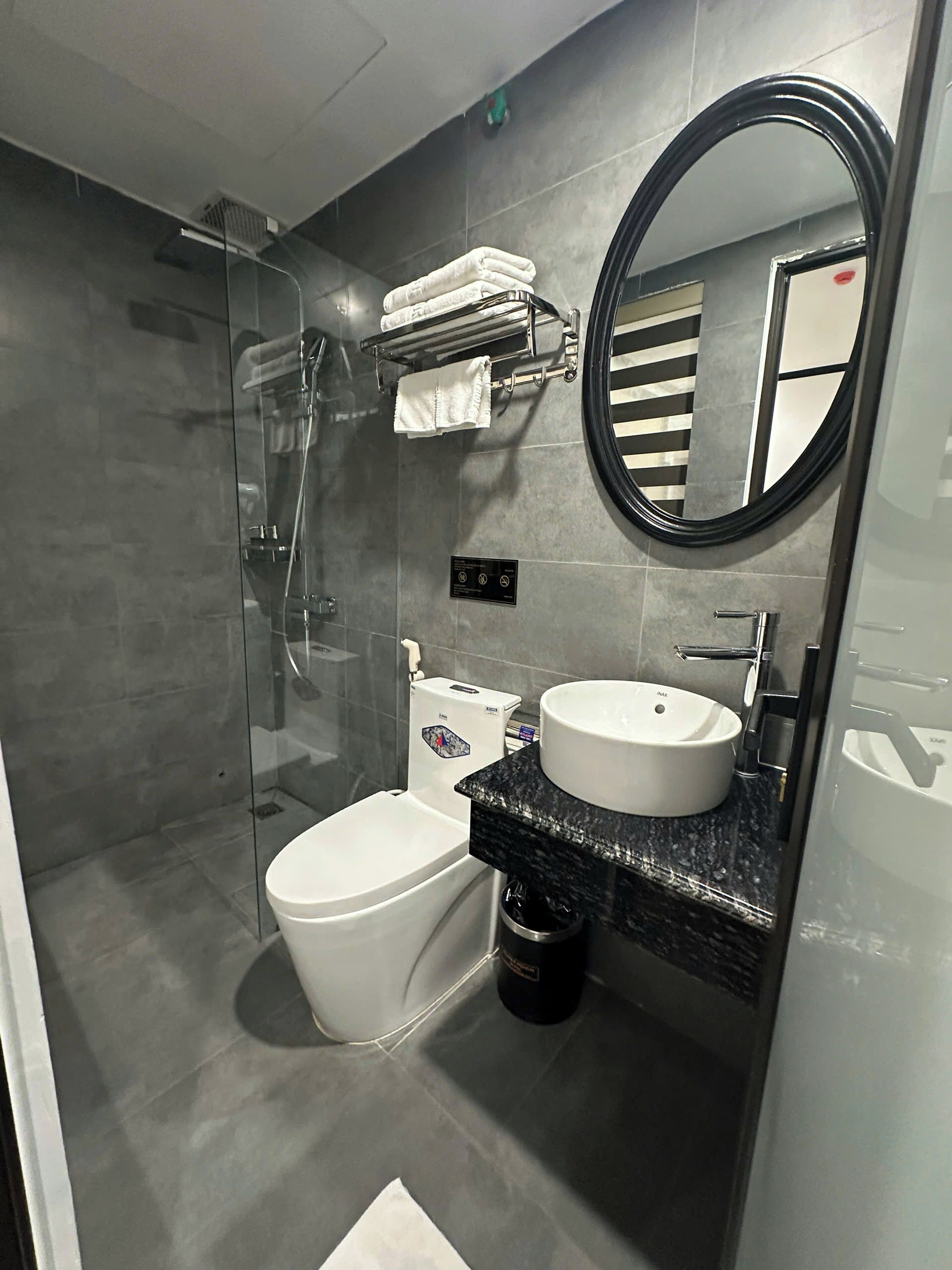 A modern bathroom with a glass-enclosed shower, a toilet, a sink with a marble countertop, and a mirror.