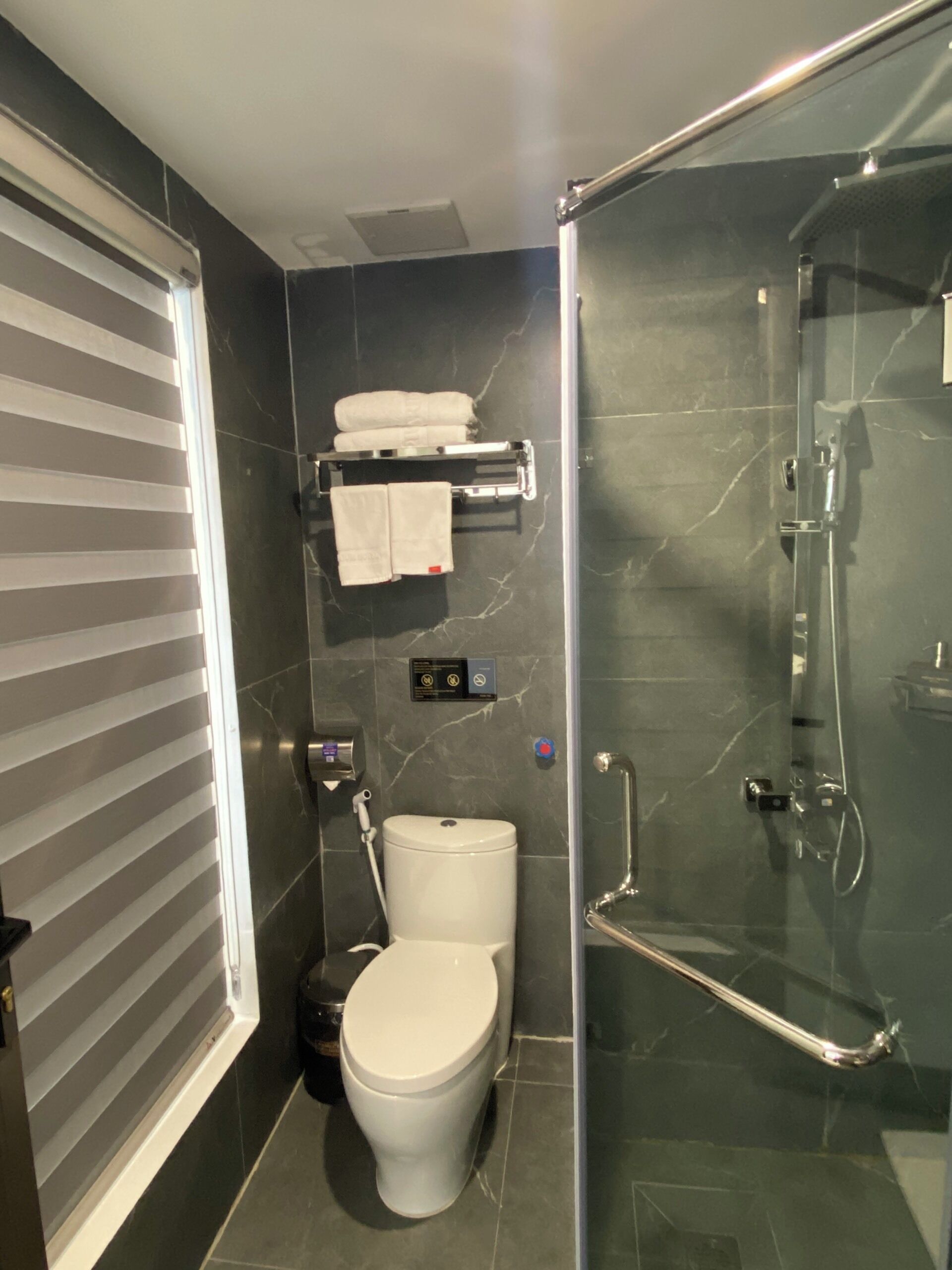 Un baño con inodoro, cabina de ducha de vidrio y un perchero con toallas.