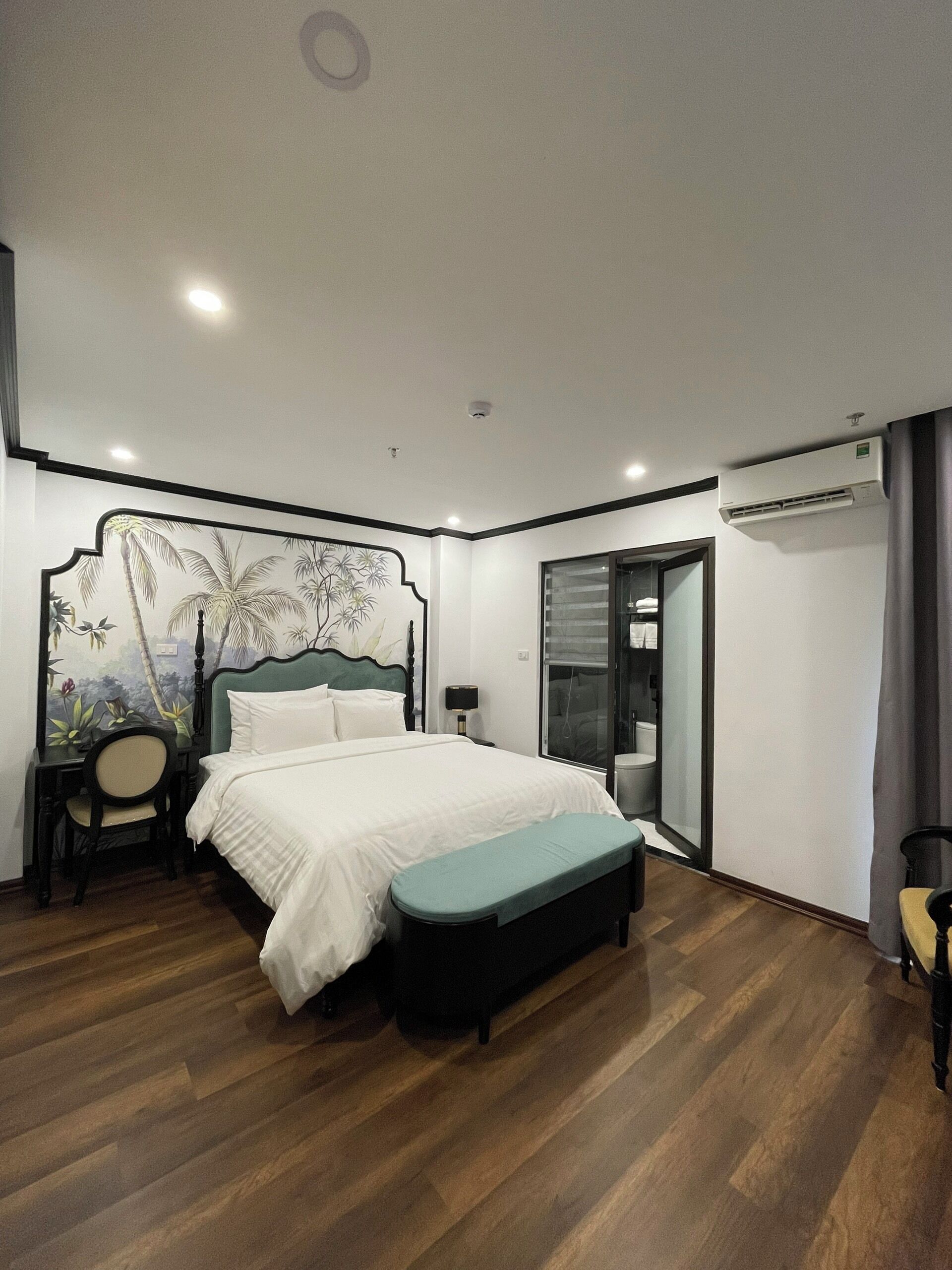 A bedroom with a bed, a desk, a chair, a bench, and an air conditioning unit.