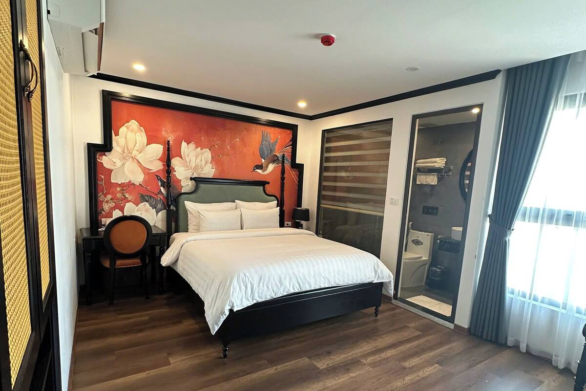 A bedroom with a bed, a nightstand, a chair, a painting, and a sliding door leading to a bathroom.