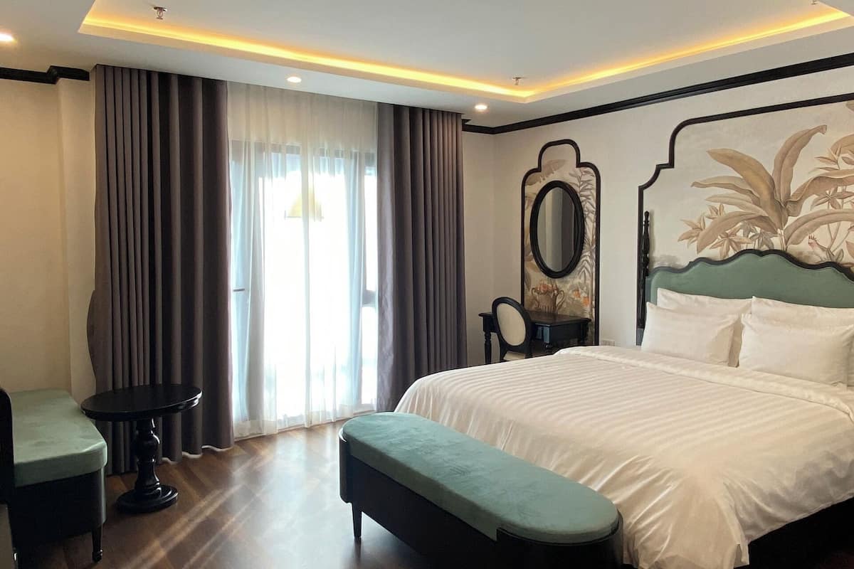 A modern hotel room with a large bed, a small round table, and a bench.