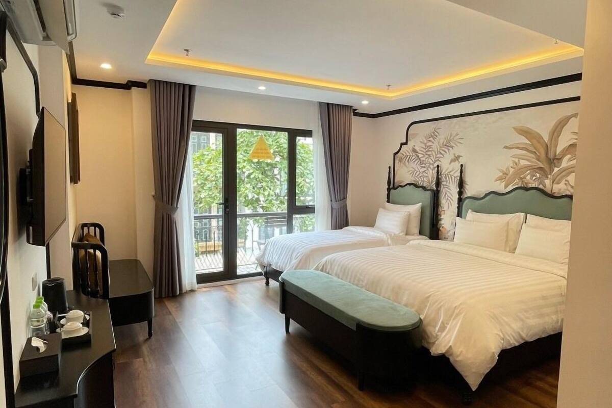 A modern hotel room with a large bed, a desk, and a view of greenery outside.