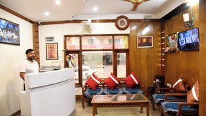 A reception area with a reception desk, seating area with sofas and armchairs, a clock, and a television screen. - Hotel Sunshine (Gurugram)