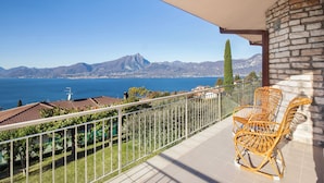 A balcony with wicker chairs, a view of the sea, mountains, and a stone wall. - Villa Teresa-Lake View (Torri del Benaco)