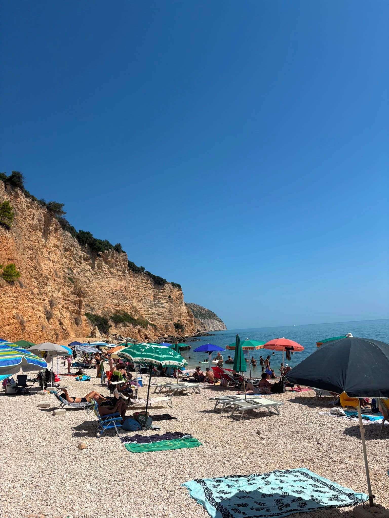 Une plage avec des parasols, des chaises longues et des gens.