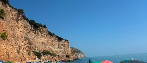 Une plage avec des parasols, des chaises longues et des gens.