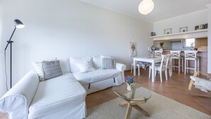 A modern living room with a white sofa, a glass coffee table, and a dining area with white chairs and a table. - City & Sea view apartment, Meia Praia Lagos (Lagos)
